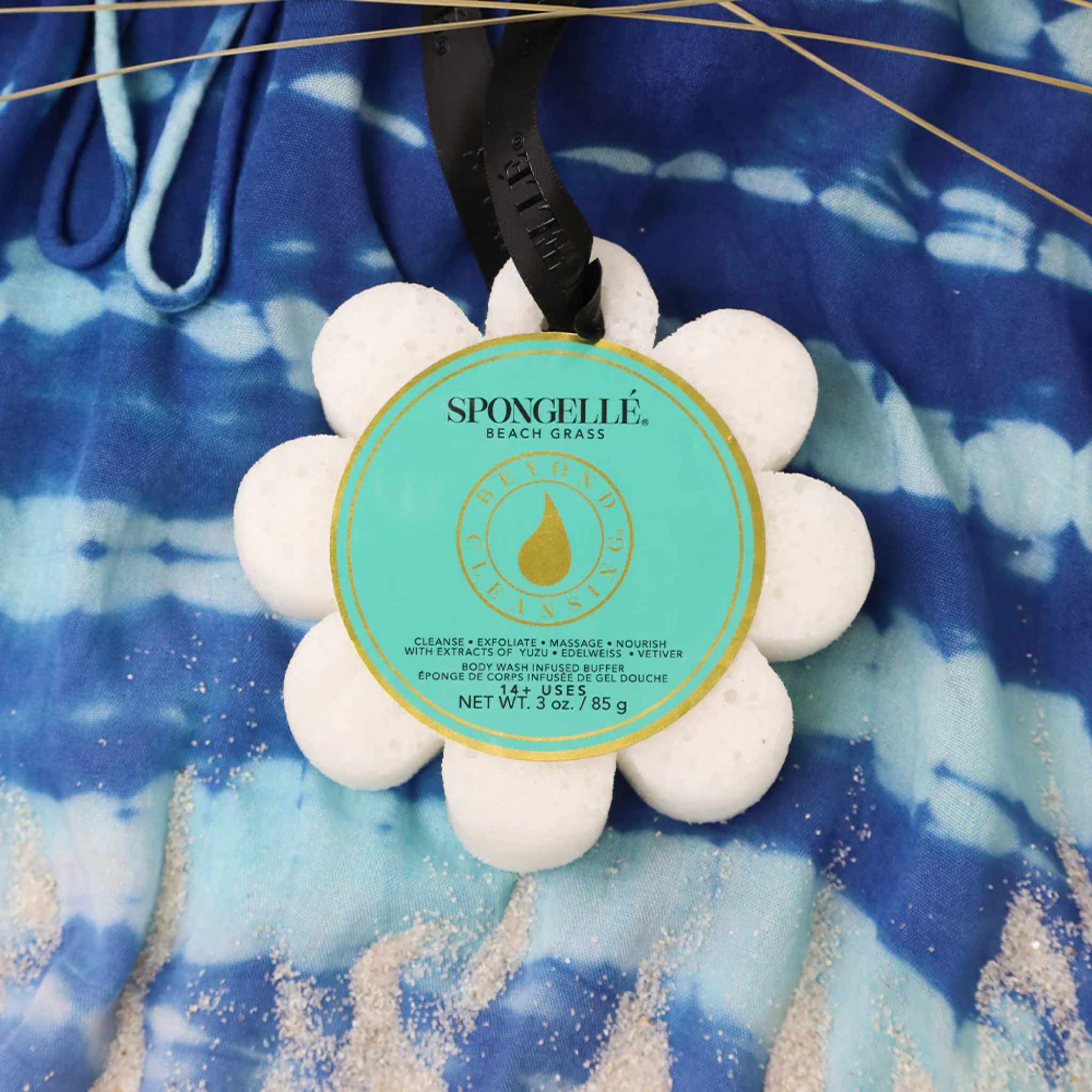 A Spongelle Beach Grass sponge against a blue tie-dye beach towel with sand on it