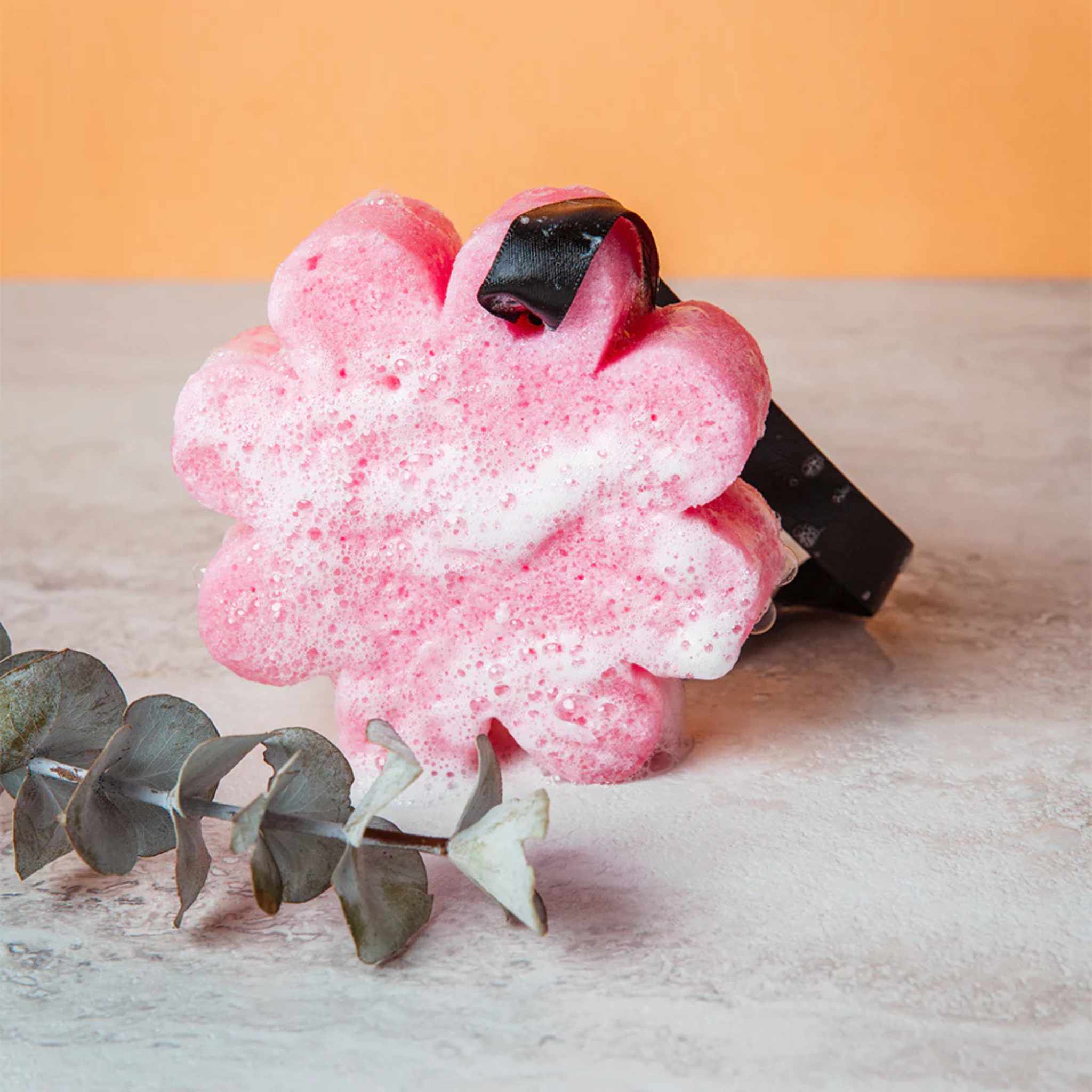 A pink flower shaped sponge with a eucalyptus branch in front of it