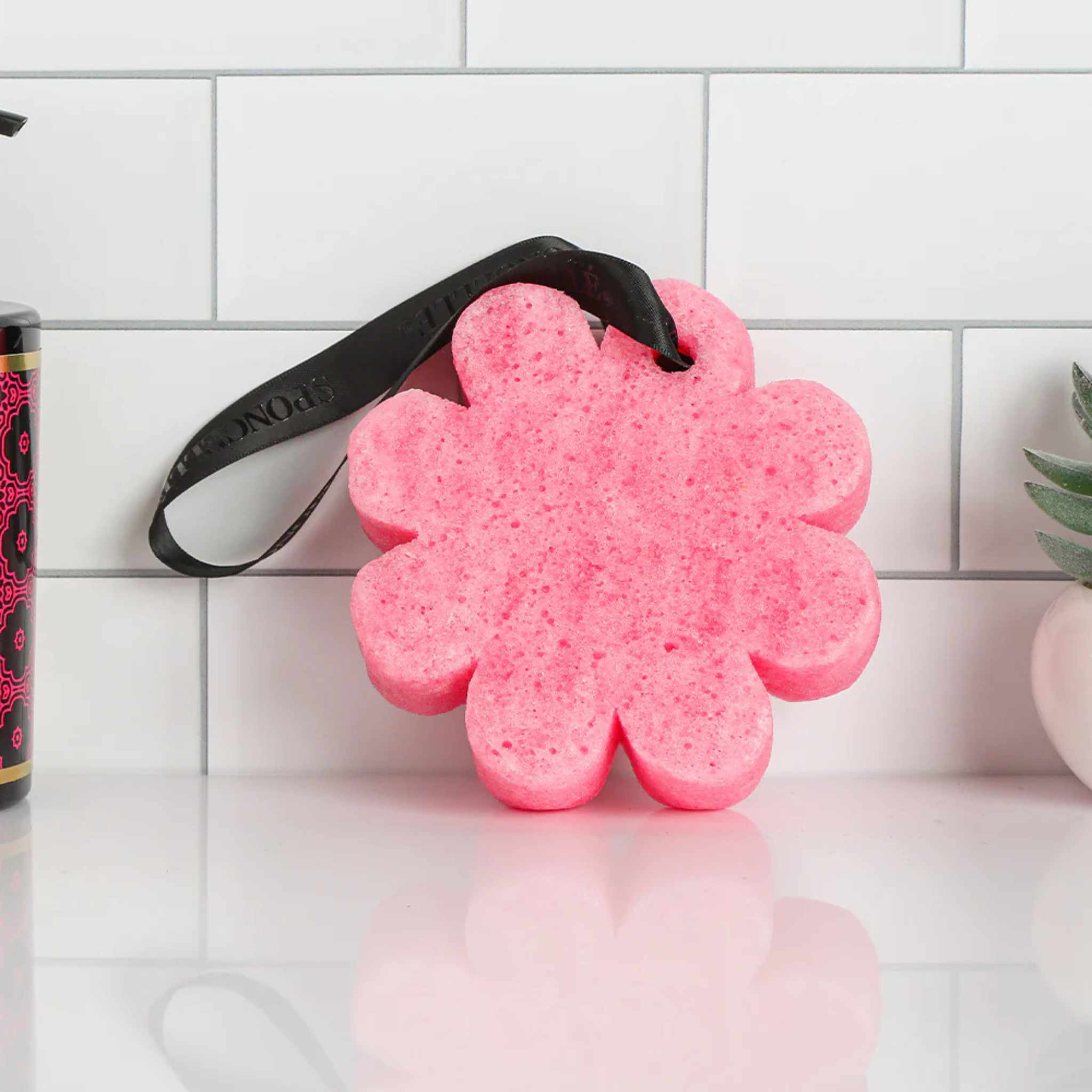 A pink flower shaped sponge leant against a white tile wall