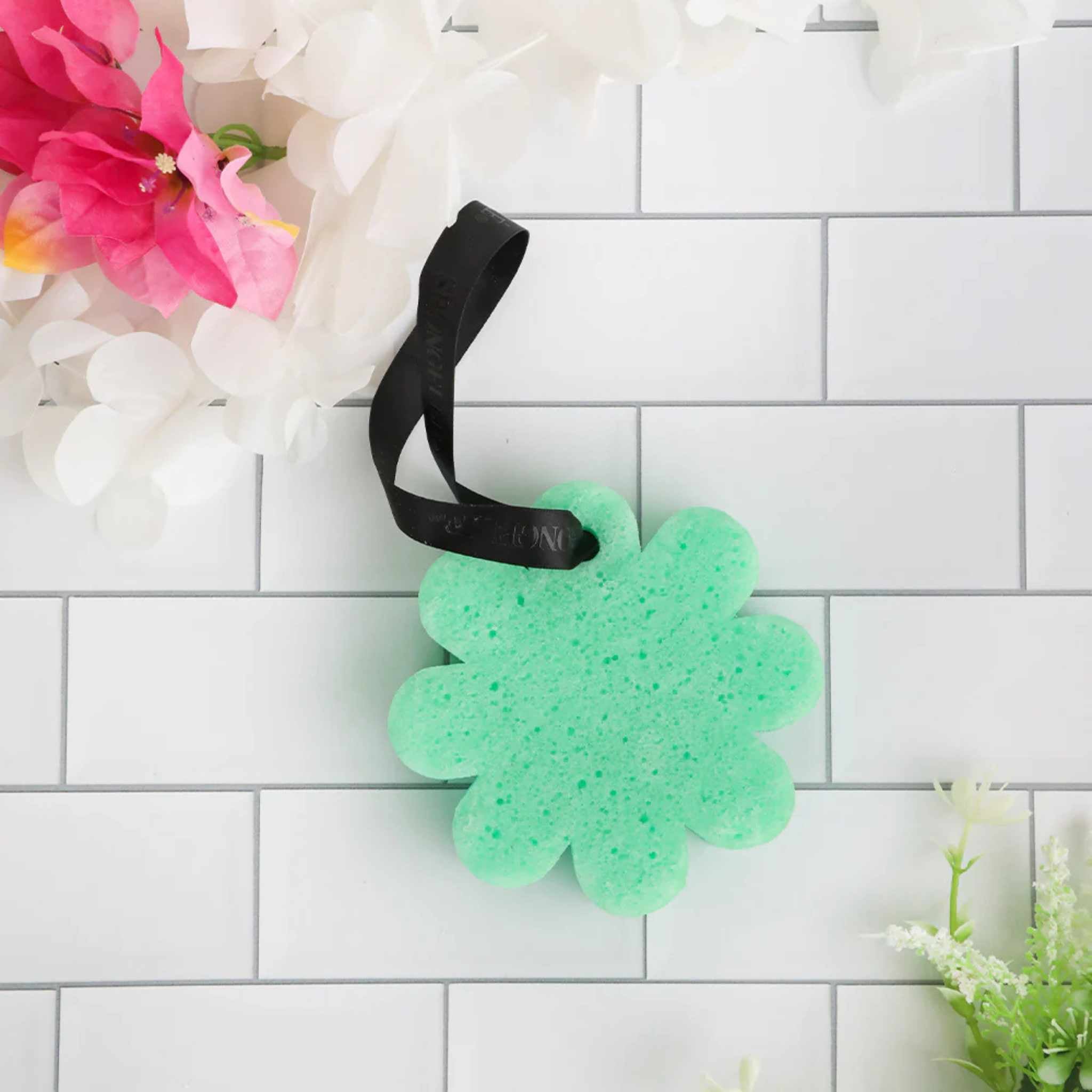 Flower shaped teal spong on white tiled background