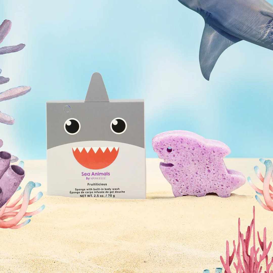 A purple bath sponge designed to look like a shark, with a packaging box that has &