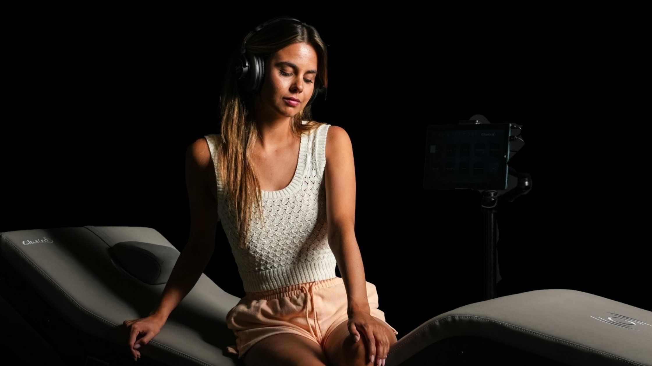 A woman wearing headphones and sat on the RLX Braingym bed