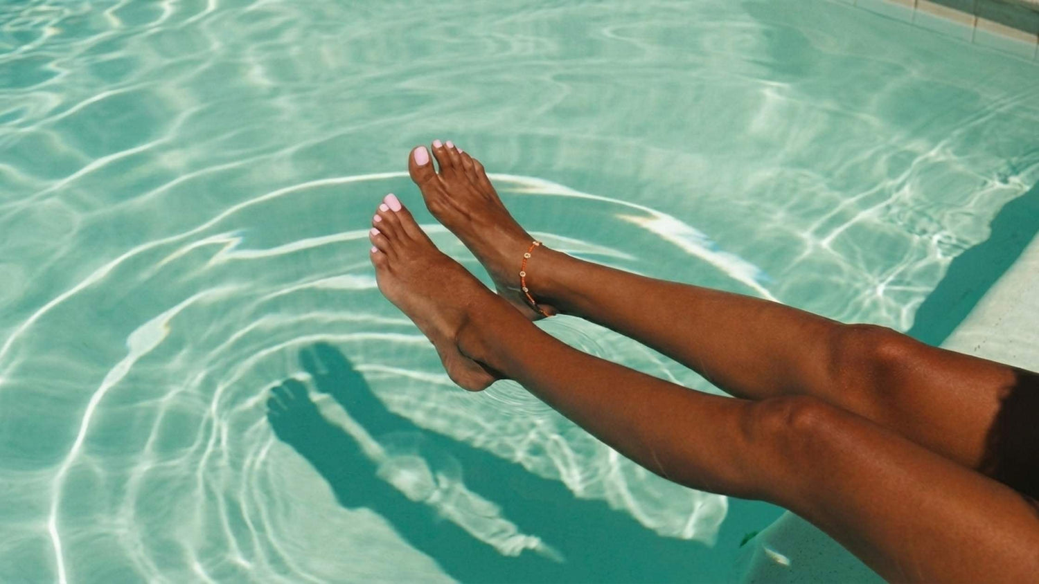 A tanned woman's legs stretched out into the pool with a light pink pedicure