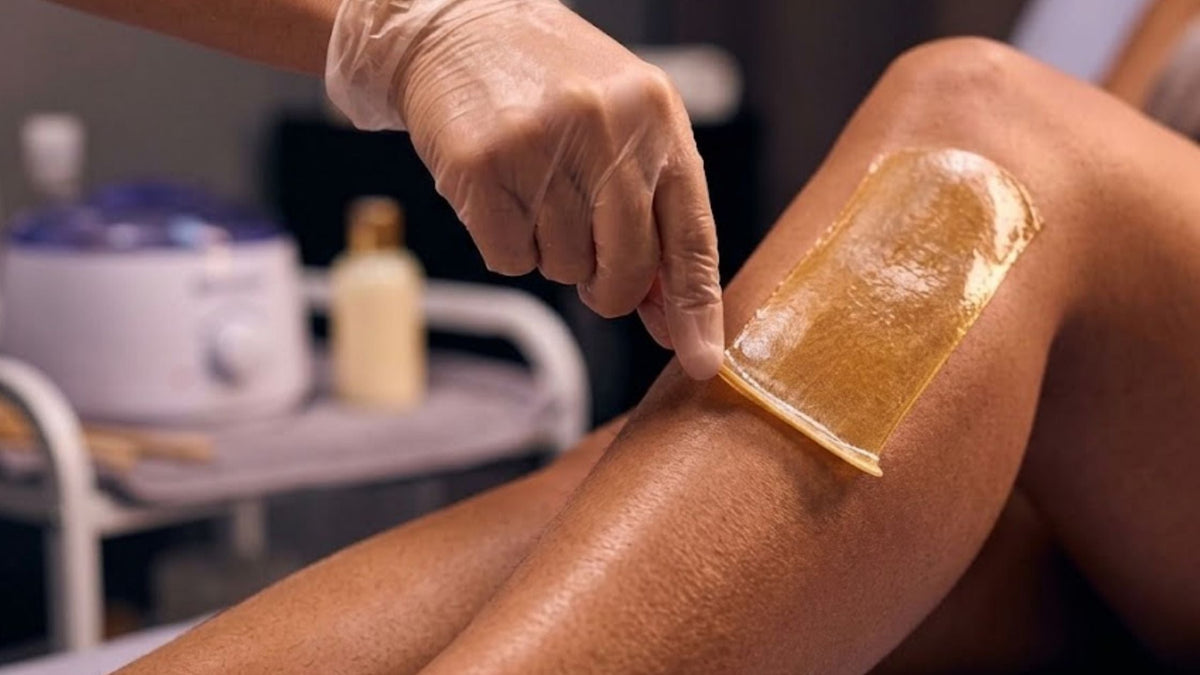 Yellow wax being applied with a wooden stick to a woman's calf
