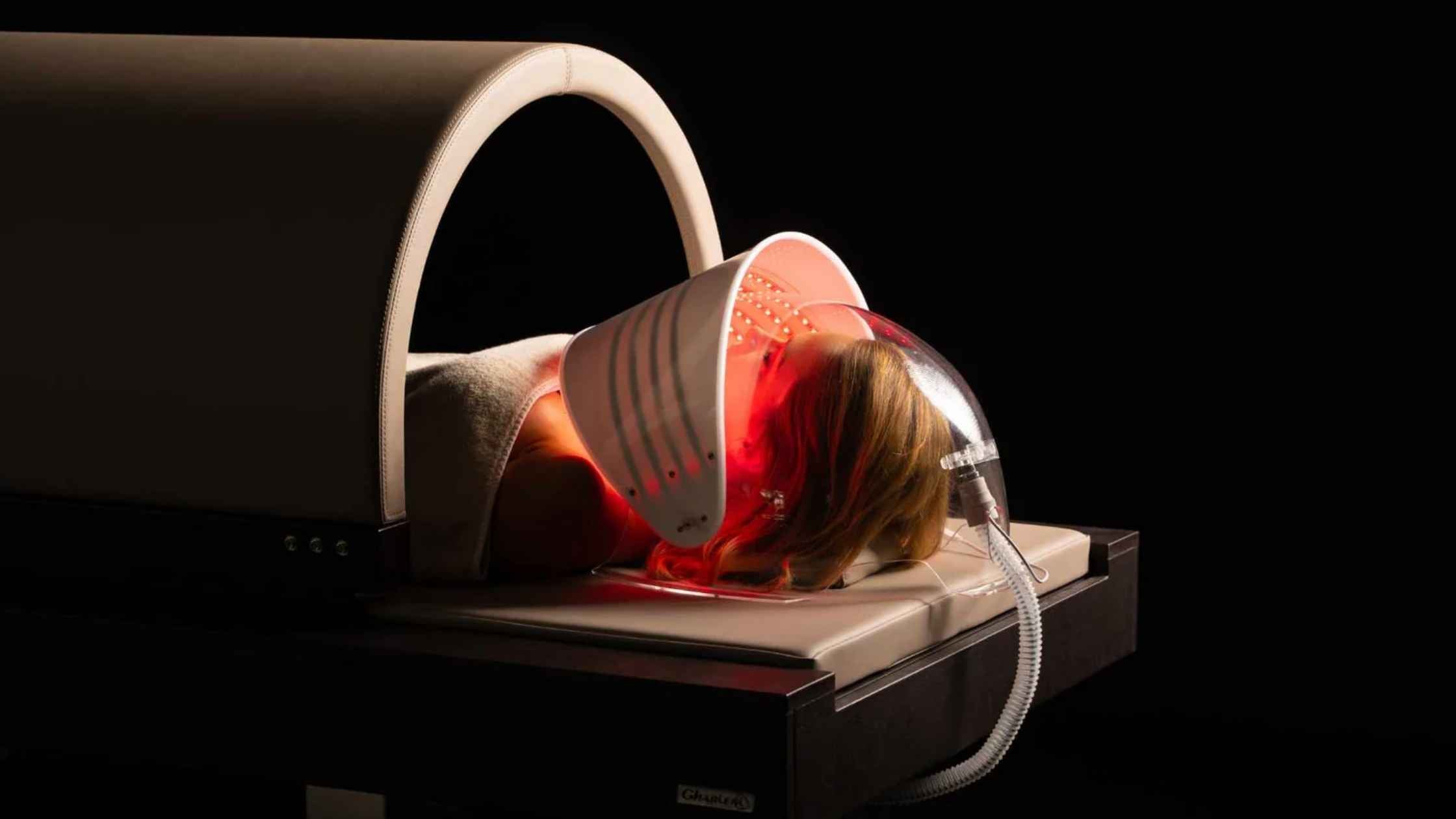 Person lying inside a cryosauna with red light therapy mask on a black background