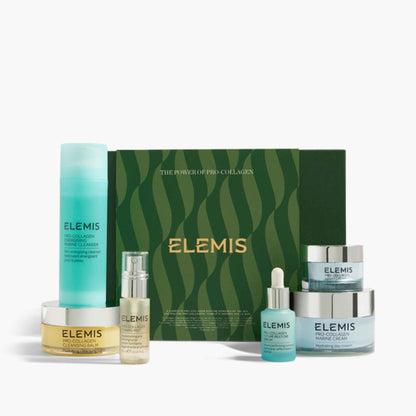 A set of ELEMIS skincare products arranged in front of a dark green patterned box. The set includes a turquoise cleanser bottle, a gold-toned serum bottle, a small turquoise dropper bottle, a light blue serum bottle, and two light blue cream jars with silver lids.